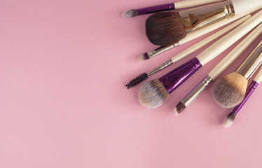 Makeup brushes on a pastel pink background. Flat lay, top view with place for text