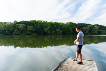 Fototapeta premium Man fishing on the pier. Fishing on the river on a sunny day. Autumn predator fishing