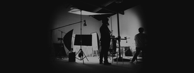 Behind the scene of photo shooting and production set up in the big studio. Professional crew team working and camera equipment in silhouette. such as light box, tripod, flashlight. and copy space.