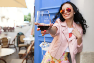 attractive young woman drinking wine on summer vacation sitting in city street cafe in cool outfit dressed in pink jacket smiling happy having fun wearing sunglasses positive mood