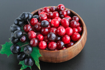 Cranberries and chokeberry in wooden bowl on black background. Nature, autumn, crop, food, berry concept.