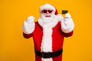 Portrait of his he nice attractive cheerful cheery fat Santa holding in hand bank card celebrating having fun safe shopping isolated bright vivid shine vibrant yellow color background