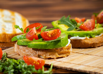 Avocado mash and fresh sliced tomatoes on grilled toast bread on brown wooden background. Trendy and healthy breakfast.