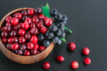 Cranberries and chokeberry in wooden bowl on black background. Nature, autumn, crop, food, berry concept.