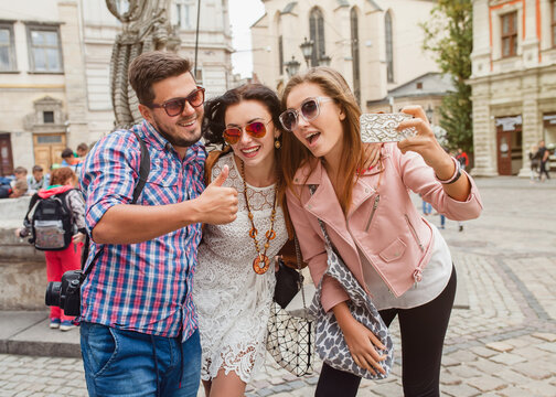 young hipster company of friends traveling, vintage style, europe vacation, sunglasses, old city center, happy positive mood, smiling, embracing, making selfie photo on smartphone