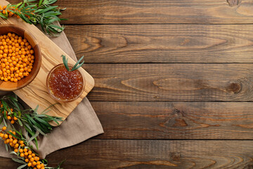 Sea buckthorn jam and sea buckthorn branches with berries on wooden table. Flat lay composition, top view.