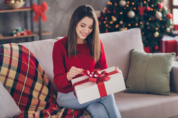 Photo of positive girl sit couch open x-mas gift box wear red sweater in house indoors with x-mas atmosphere ornament