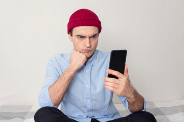 Thoughtful man is reading sms on phone, person is sitting at home, portrait