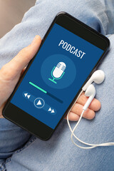 The phone with the podcast turned on lies in a woman's hand against the background of jeans....