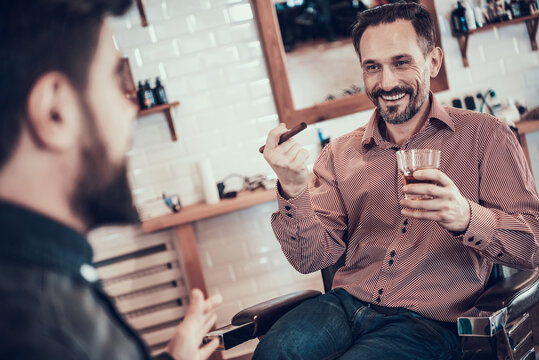 Man with cigar and whiskey sits in barbershop. 