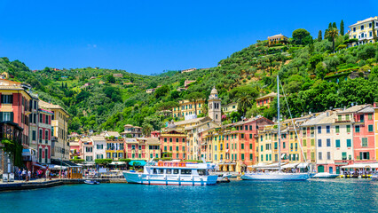 Fototapeta na wymiar Portofino, Italy - Harbor town with colorful houses and yacht in little bay. Liguria, Genoa province, Italy. Italian fishing village with beautiful sea coast landscape in summer season.