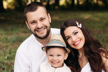 Stock photo headshot of a lovely Caucasian family of mother, father and their son smiling happily at camera in the park on summer day.