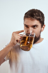 A bearded man with a mug of beer on a light background in a white T-shirt cropped view of an alcoholic drink