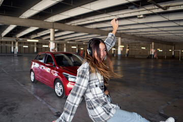 Young woman dancing and jumping in front of her car in a parking lot.