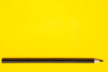 horizontal black sharp wooden pencil on a bright yellow background, isolated, copy space, mock up.