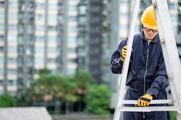 Asian maintenance worker man wearing protective suit and safety helmet adjusting aluminium step ladder at construction site. Civil engineering, Architecture builder and building service concepts