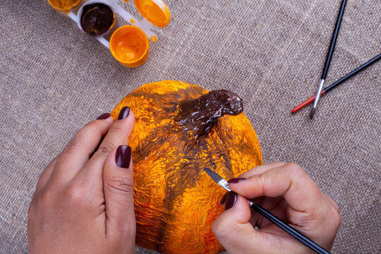 hands paint a homemade papier mache pumpkin in orange for an autumn holiday, a hobby for children.