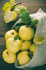 Top view of ripe quinces rolling out of a linen sack, brown wooden background, vertical stock photo