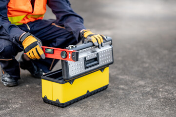 Male mechanic or maintenance worker man holding red aluminium spirit level tool or bubble levels opening tool box at construction site. Equipment for civil engineering project
