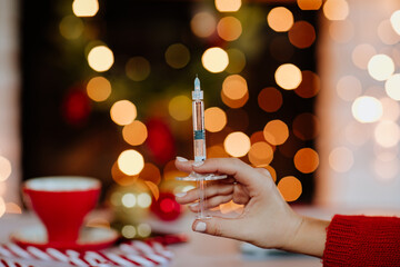 Woman's hands holding medical syringe against Christmas background.