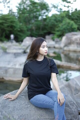 Stylish blonde girl wearing a black shirt with views of natural rocks, lake water and clear sky. female t-shirt models for mockups and templates.