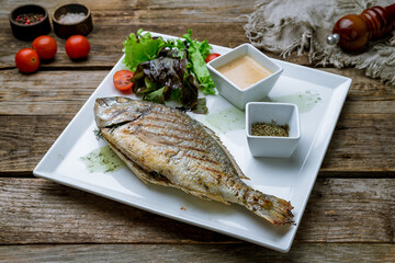 Dorado on grill on a white plate on old wooden table