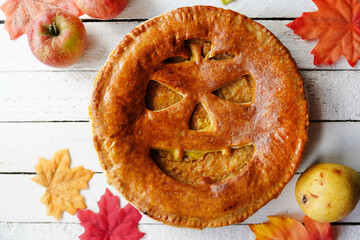 Delicious homemade pie for halloween on white wooden table with apples and fall leaves