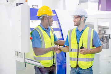 Two factory worker men with uniform shaking hands also smiling and look to each other in front of machine. Concept of good management system to support industrial business working.