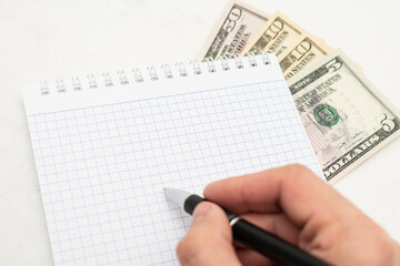 USA dollars and notebook, man's hand with pen, white background, copy space, top view