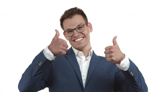 Young happy businessman in blue suit and glasses jumping from bottom, appear with thumbs-up and smiling, praising something very good, standing over white background