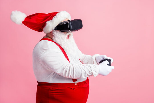Profile side view portrait of his he addicted bearded fat overweight Santa wear vr helmet gadget device hi-tech realistic playing console watching air blow wind isolated pink pastel color background