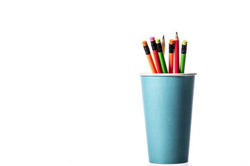 Disposable coffee cup as pencil holder. Bunch of multi colored wooden pencils with rubber eraser in blue disposable biodegradable paper cup copy space isolated on white background. Recycling concept.