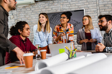 Group of young business people in casual wear discussing architectural designs while sitting in the creative office.