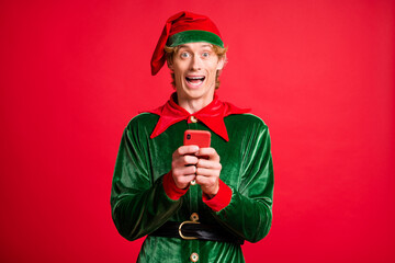 Photo of excited funky elf guy hold cellphone x-mas christmas discounts wear green cap isolated over red color background