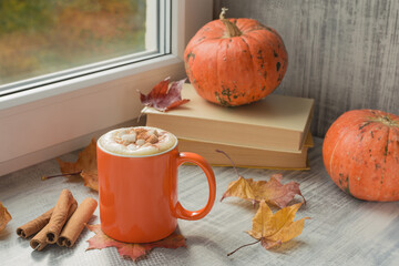 Bright orange mug of latte with whipped cream, marshmallow, spices and fall decor. Traditional Coffee Drink for Autumn Holidays.