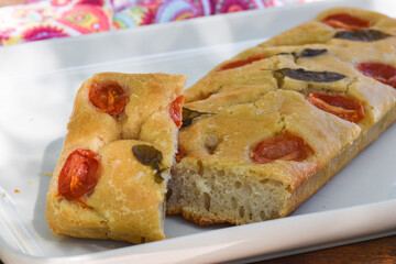 focaccia de tomates e manjericão sobre parto branco ao ar livre.