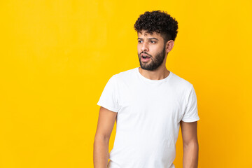 Young Moroccan man isolated on yellow background doing surprise gesture while looking to the side