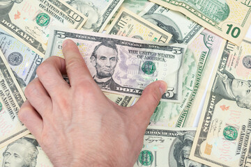 Hand takes a five-dollar bill, dollar bills in the background, a man's hand, close-up