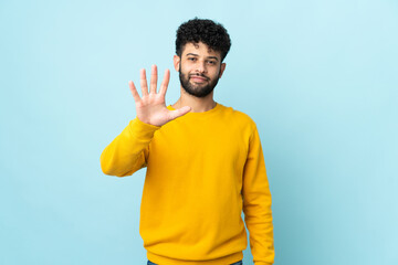 Young Moroccan man isolated on blue background counting five with fingers