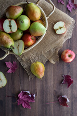 Top down view of a basket filled with apples and pears surrounded by dried leaves. Autumn concept.