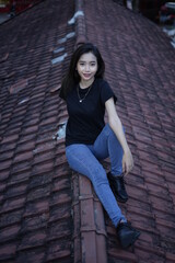 The blonde girl sits on the roof tile while stylish wearing a black t-shirt. female t-shirt models for mockups and templates.