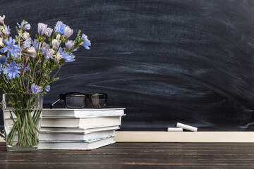 Flowers in a glass cup, books, glasses and calendar with the date of October 5, against background of chalkboard, Teacher's Day concept. Copy space.