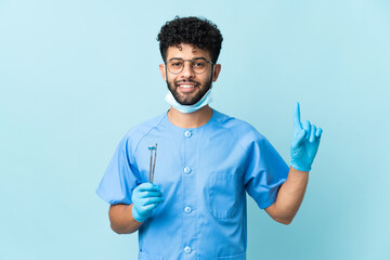 Moroccan dentist man holding tools isolated on blue background pointing up a great idea