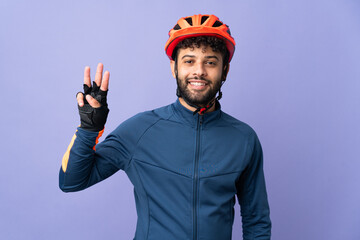 Young Moroccan cyclist man isolated on purple background happy and counting three with fingers