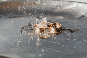 wedding rings on a chrome plated surface. water drops with reflections of light. water splashes