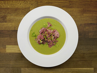 Luxury creamy pea soup with pork on a wooden background