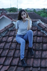 The blonde girl sits on the roof tile while stylishly wearing a gray shirt. female t-shirt models for mockups and templates.