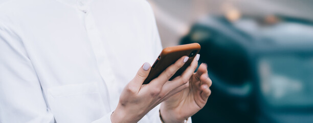 Crop young satisfied woman using smartphone in street