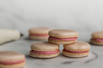 Homemade raspberry macarons stacked on white marble background. 
