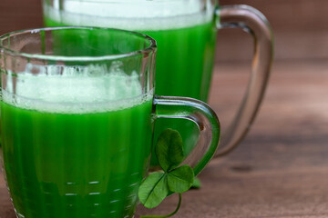 Shamrocks clovers on wooden table with a two mugs of green beer.